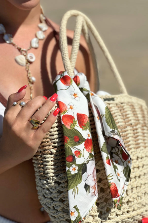Cesto de palha à beira-mar com lenço de limões removível, segurado por uma mão com pulseira delicada.